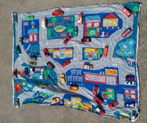 Toy cars arranged on fabric with pictures of roads and buildings.