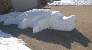 Snow sculpture of alligator on concrete driveway.