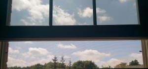 Open window with view of treetops and small white clouds.