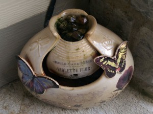 Ceramic garden fountain with pebbles at the top, covered with algae.