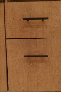 Two sturdy black drawer pulls on a wooden desk.