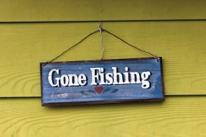 Wooden sign "Gone Fishing" hanging on a wall with wooden siding.