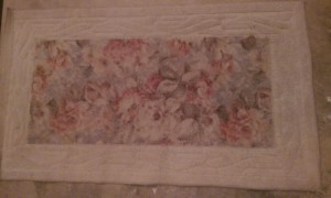 Faded off-white rectangular rug with a floral pattern in the middle.