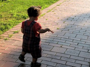 Toddler taking steps on a brick walkway.