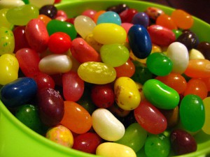 Jellybeans of different colors in a green plastic bowl.