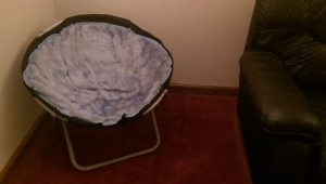 Old blue chair in corner of home theater next to black leather sofa.