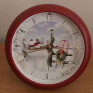 Analog clock with a red frame and a wintery holiday picture in the middle.