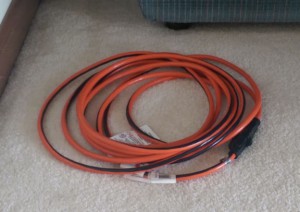 Orange electrical cord on the carpet next to the couch.