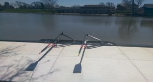 Black double scull in the river, next to a white dock.