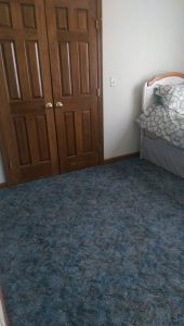 Blue carpet, just vacuumed, with closet doors and a corner of a bed in the background.