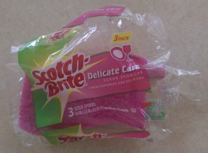 One sponge in an open pack of three Scotch-Brite "Delicate Care" scrub sponges.