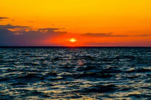 Sun setting in orange clouds over the ocean.