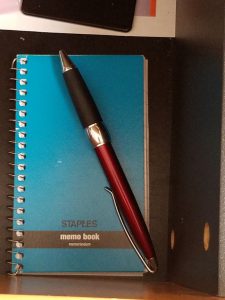 Small spiral notepad in desk drawer with pen.