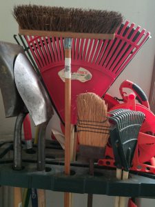 Brooms, rakes, and other tools on a rack in the garage.