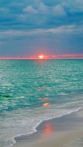 Green sea with orange sun and deep blue clouds.