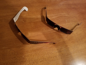 Two pairs of eclipse glasses on a wooden table.