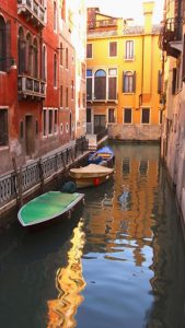 Brightly colored image of boats docked in a canal between buildings.