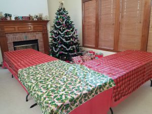 Tables pushed together, with holiday tablecloths, around the Christmas tree.