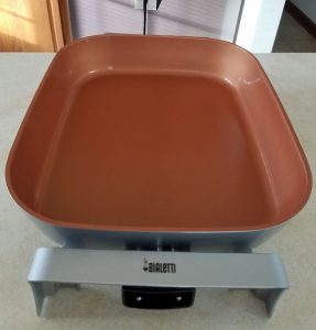 Electric skillet on kitchen counter with refrigerator in background.