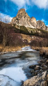 Photo of a frozen stream with bare mountains in the background.