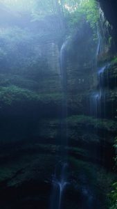 Waterfall in a cave with a forest looming overhead.