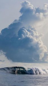 Wave cresting under a puffy cloud.