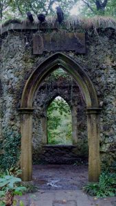 Photo of a stone doorway in an old building with a window and greenery.