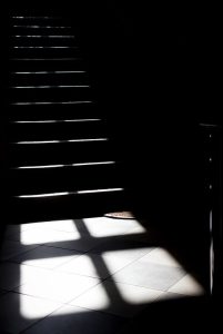 Black and white image of a dark staircase with light shining down.