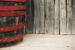 Photo of an old wooden barrel with red metal staves, on a wood floor.