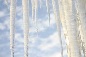 Photo of icicles with sky and clouds in background.